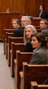 Le pesanti porte dell’aula di tribunale si aprirono con un lungo cigolio metallico che attraversò il silenzio come una lama.